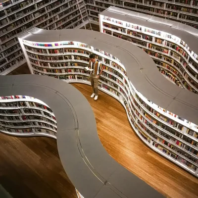 A modern library interior featuring unique curved bookshelves viewed from above, with a man reading.