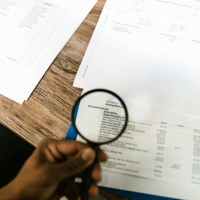 Close-up of hand using magnifying glass to review documents. Ideal for financial themes.